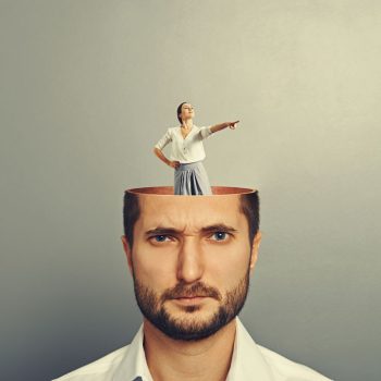30769269 - displeased businessman with open head. young smiley businesswoman standing into his head and showing the direction. photo over grey background